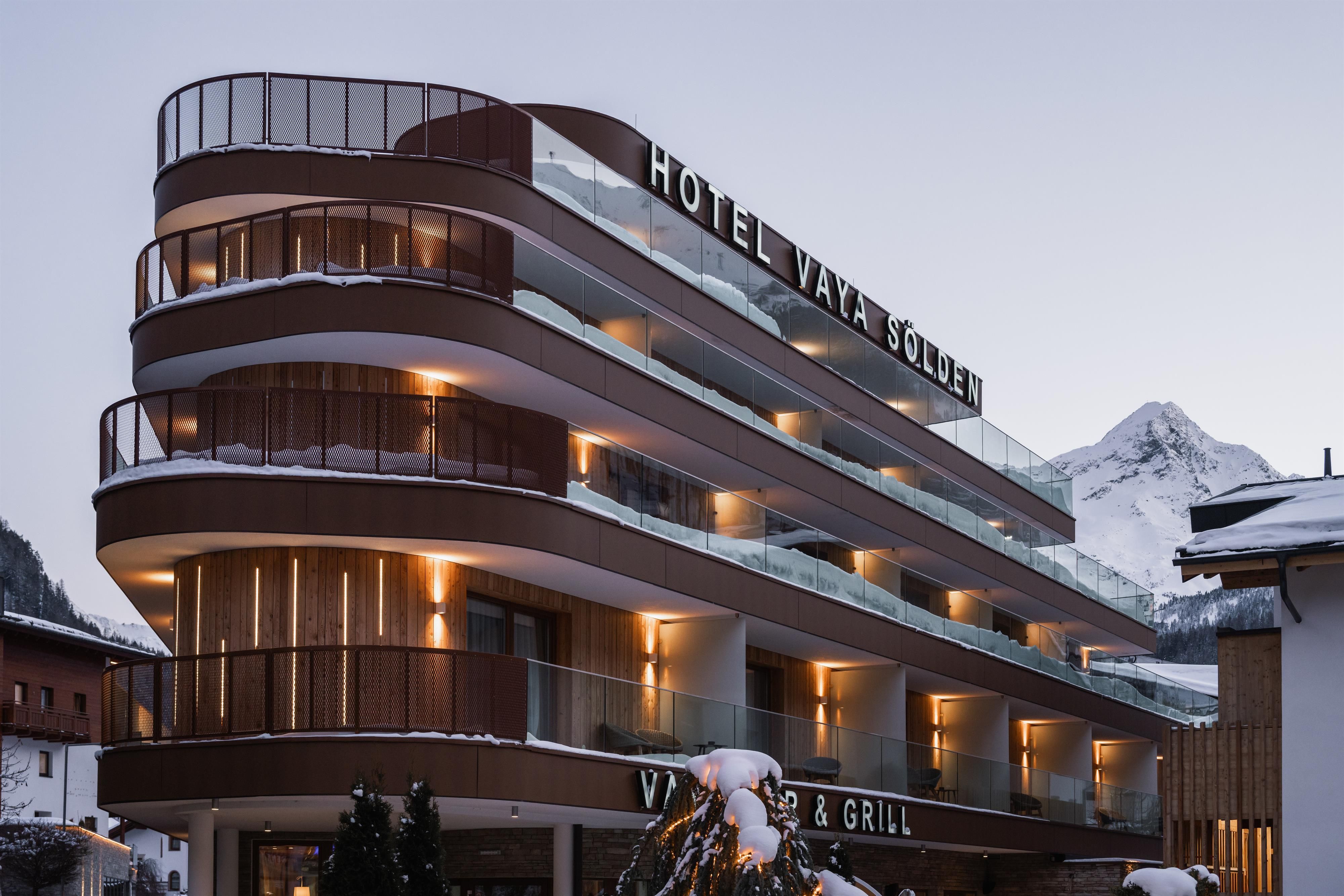 A modern hotel building named "Hotel Vals Sonet". Snow-covered mountains can be seen in the background.