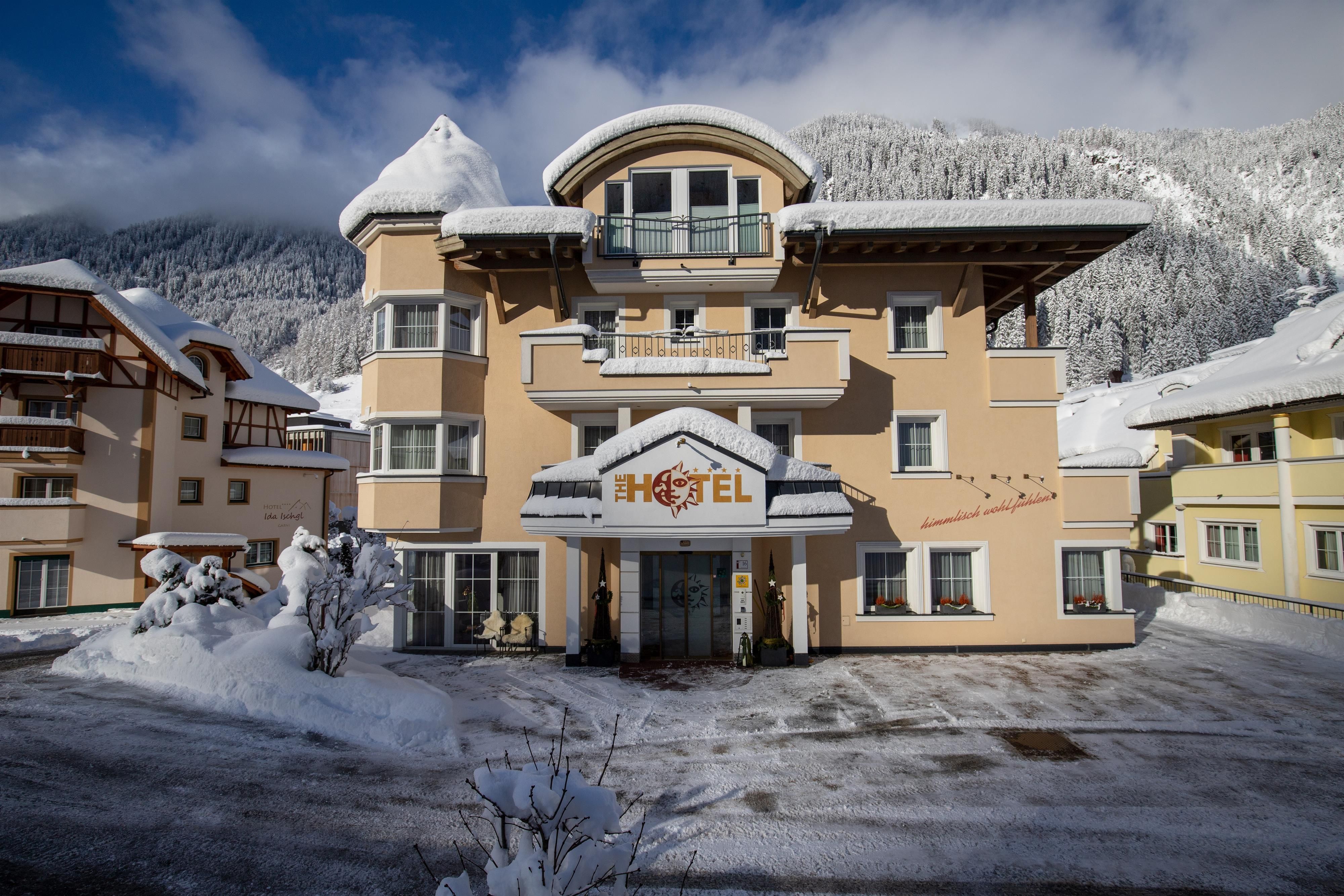 A cozy hotel in the snow, surrounded by mountains. The facade is bright with an inviting entrance area.