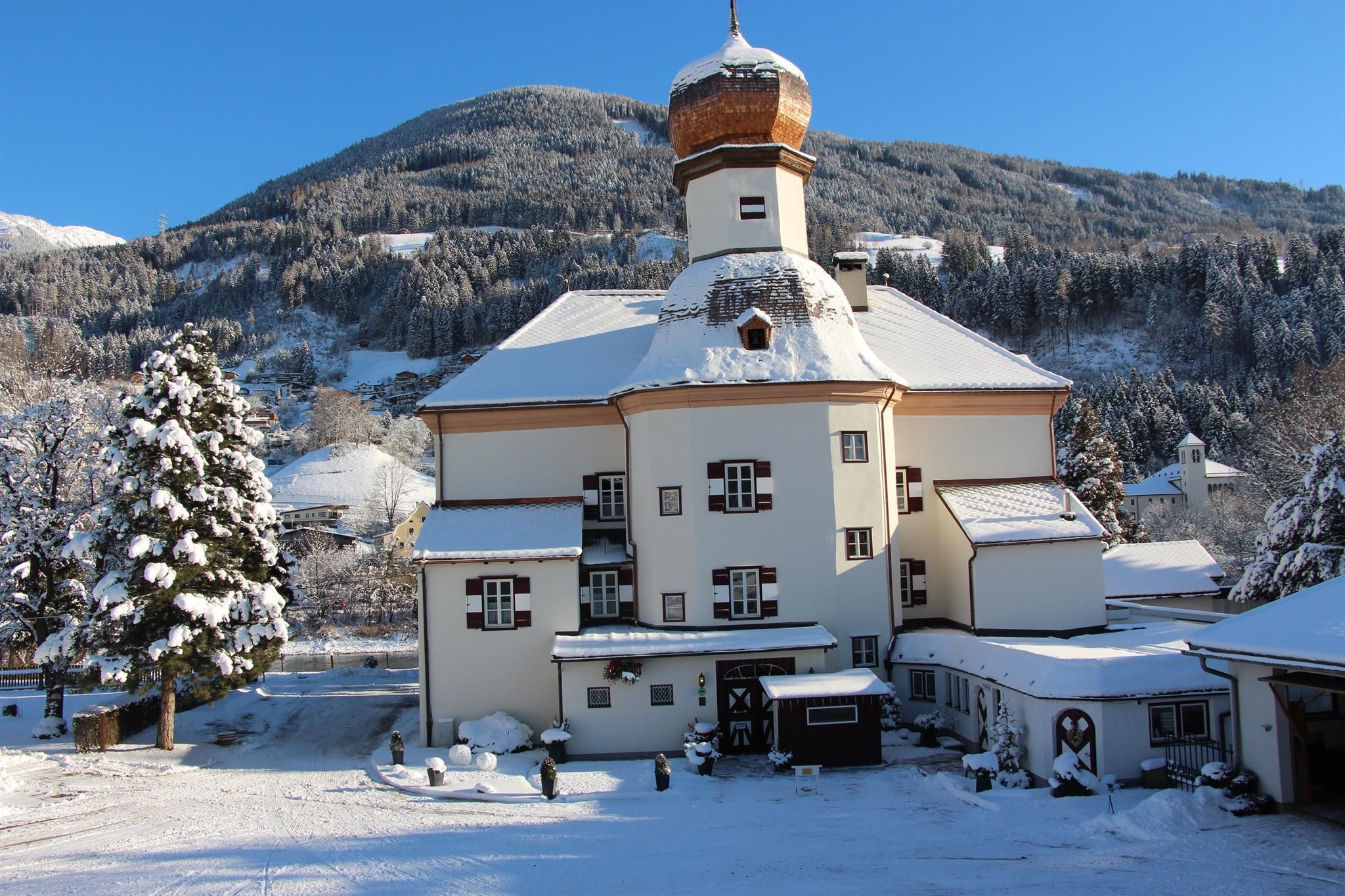 A charming building in the snow with a distinctive dome-shaped tower. In the background, snow-covered mountains and trees can be seen.