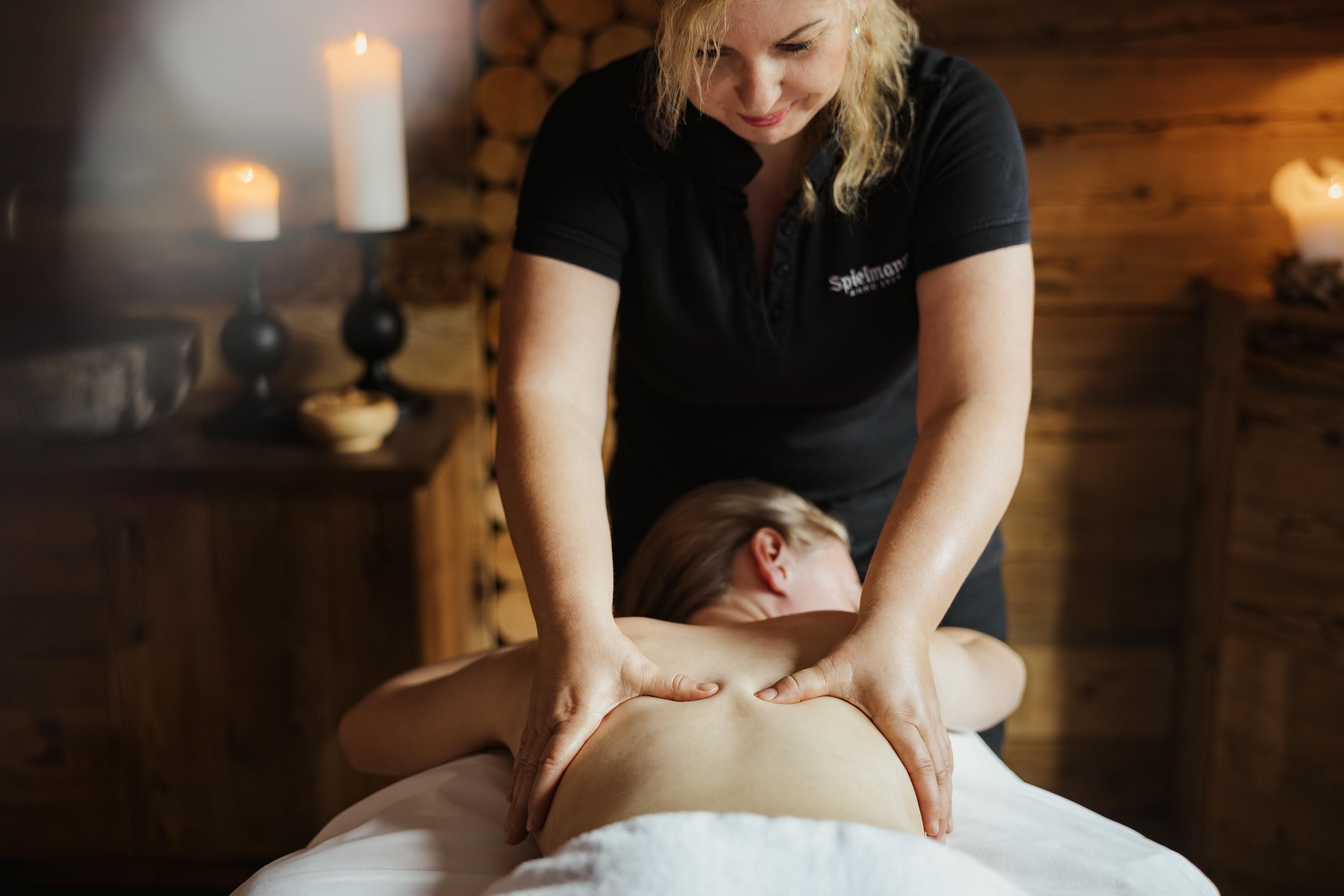 A woman is receiving a back massage in a relaxed ambiance. Soft light and candles create a calm atmosphere.