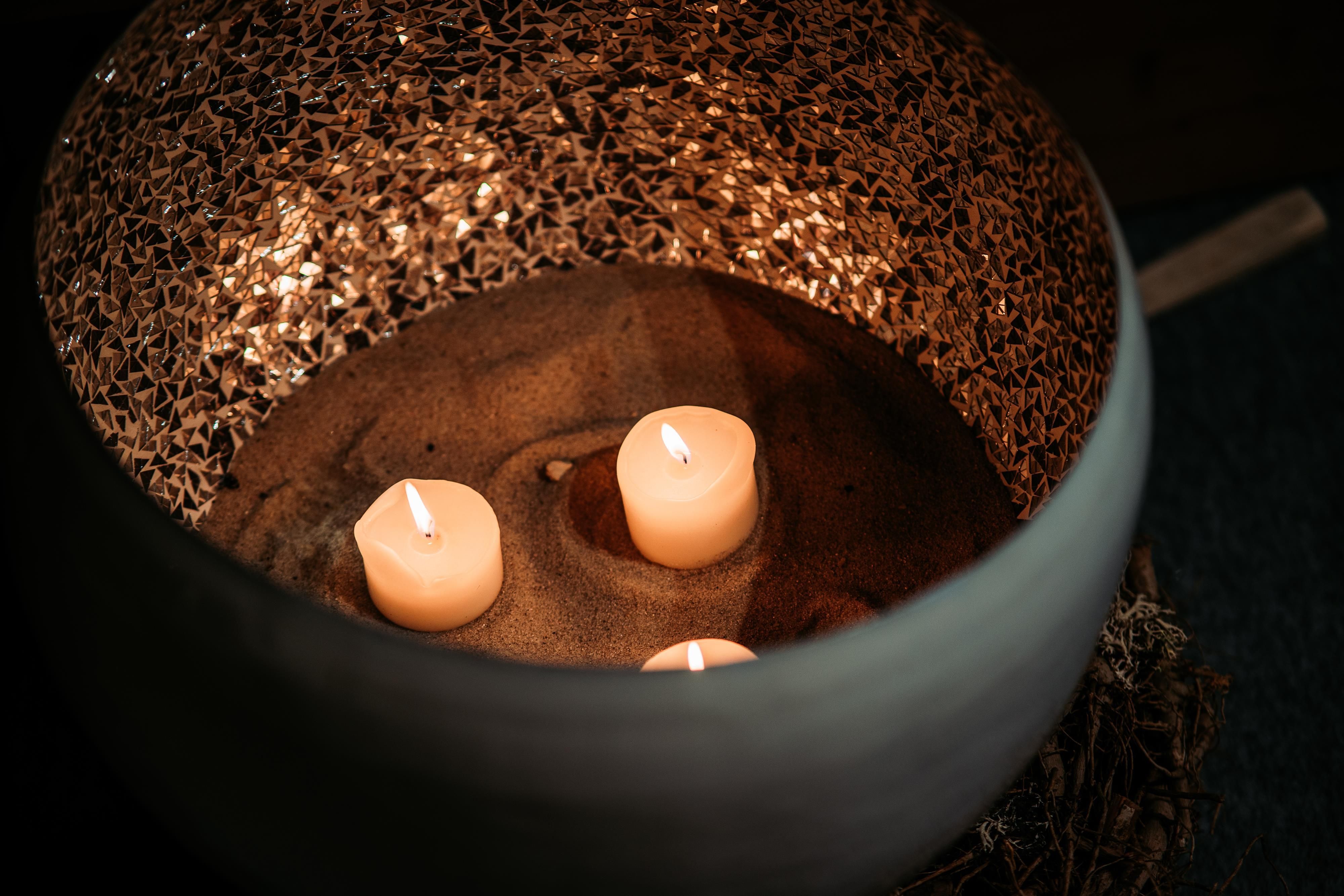 A decorative bowl with three burning candles on sand. The interior is decorated with golden material, creating a cozy atmosphere.