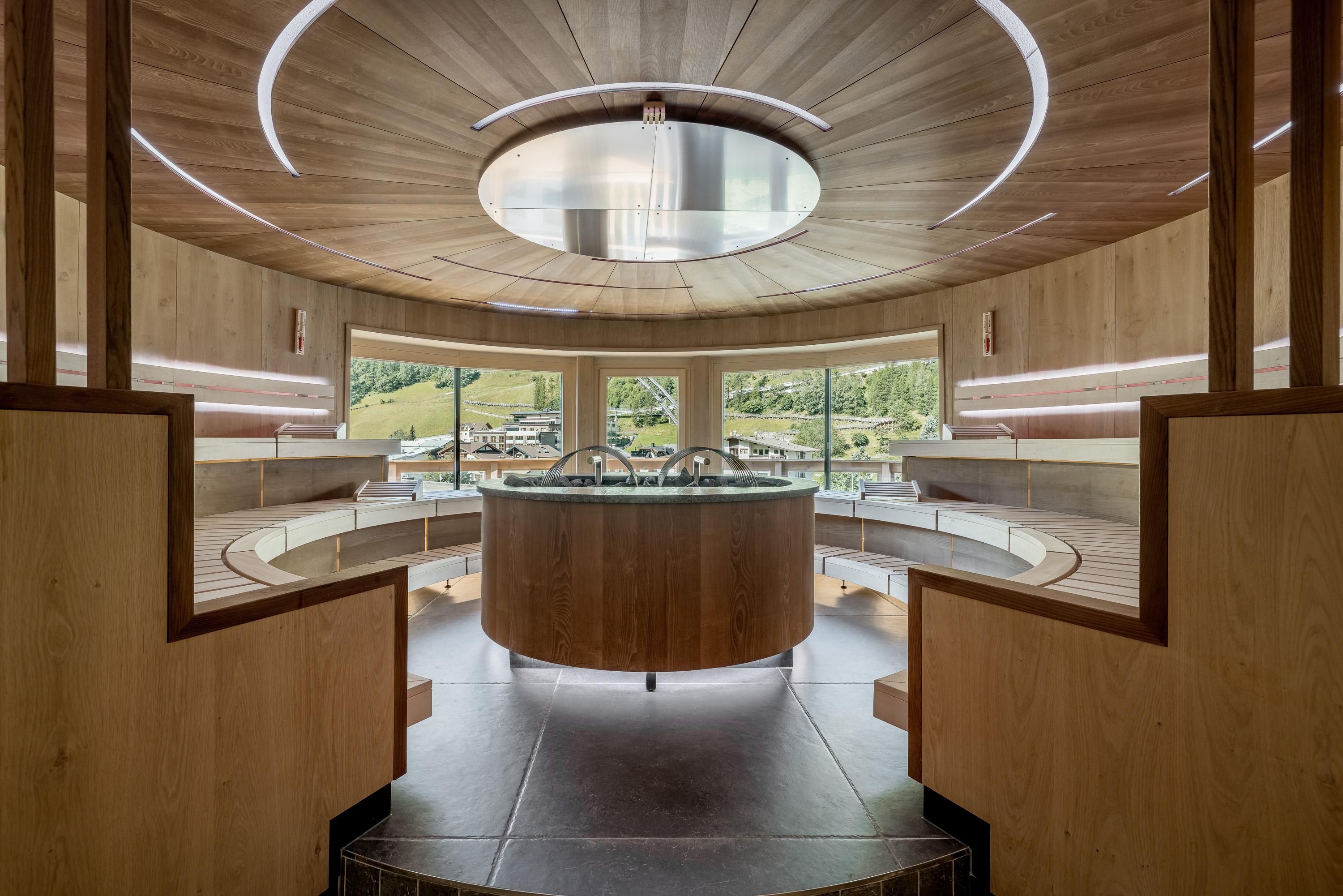 A modern spa with round wood paneling and large windows. The central area provides a peaceful viewpoint to the outside.