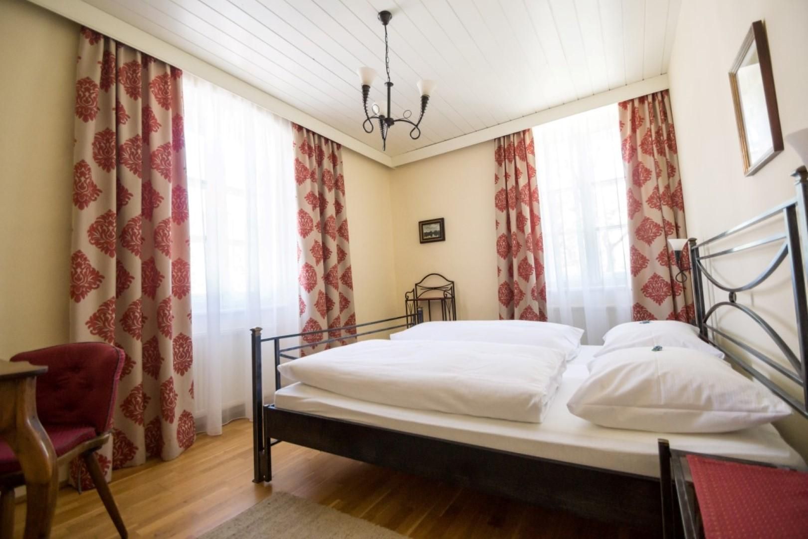 A cozy bedroom with a double bed and light curtains. There is a wooden table and chairs as well as a warm floor.