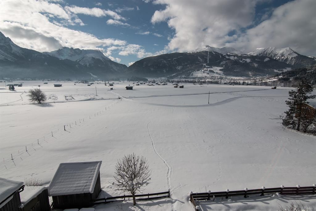 A snow-covered landscape with mountains in the background. The sky is partly cloudy, and there are a few scattered trees.