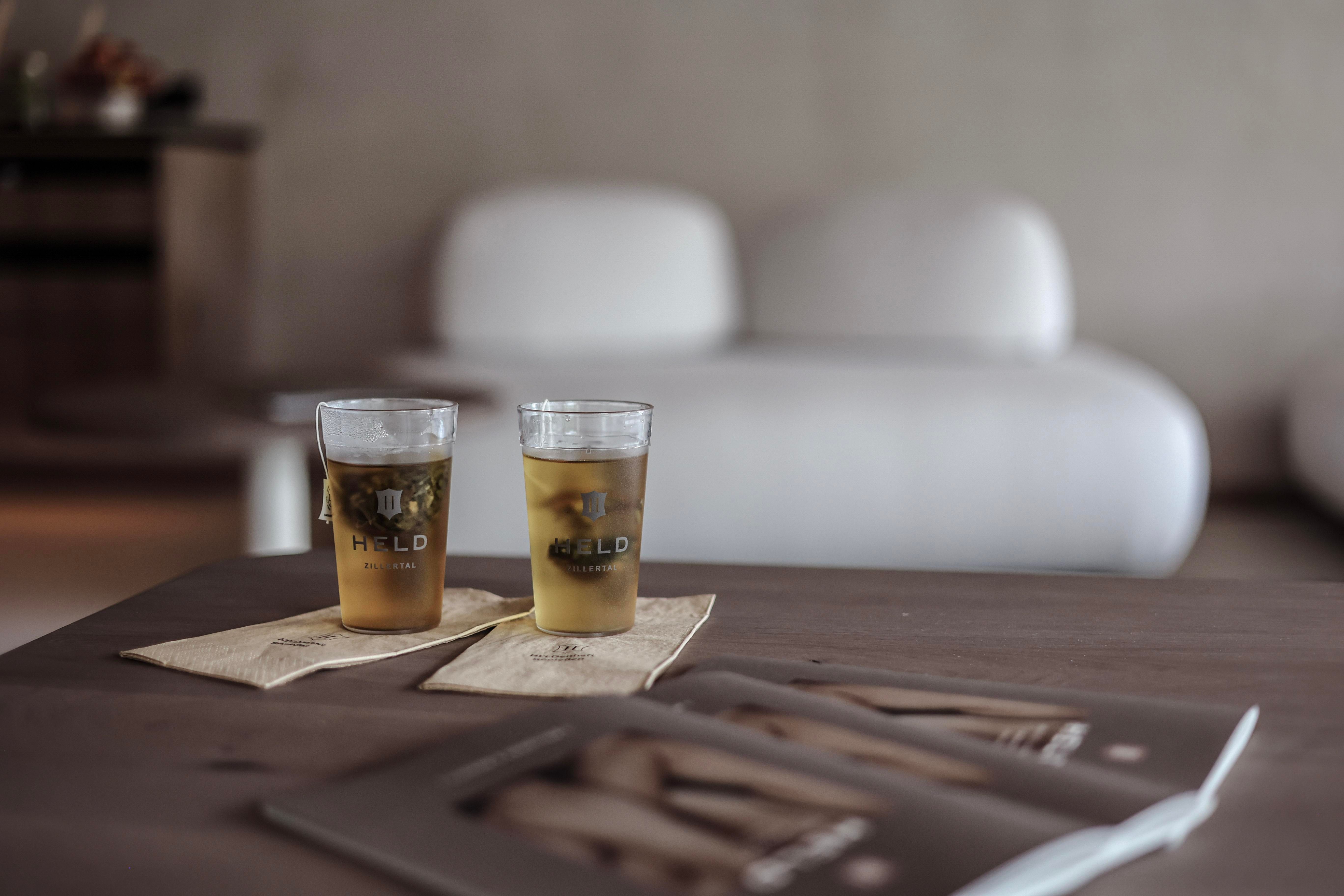 Two glasses of drinks are on a wooden table. In the background, a stylish, bright sofa can be seen.