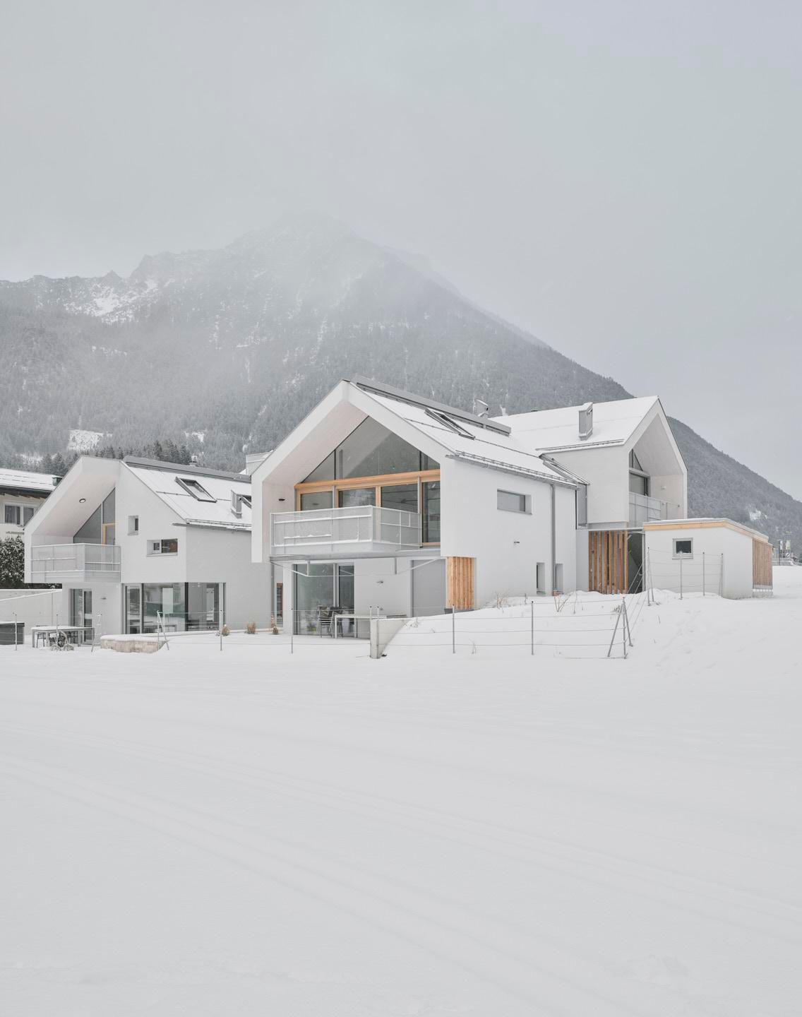 A modern, white house in a snow-covered landscape. In the background, snow-covered mountains and a gray sky can be seen.