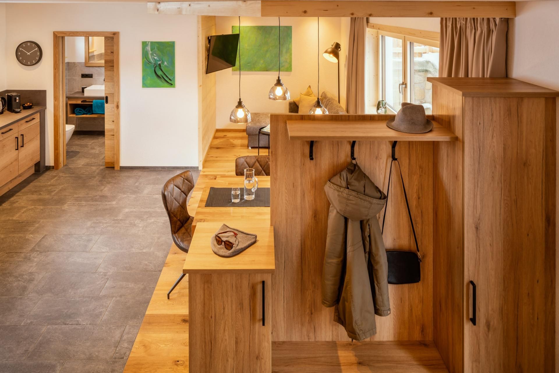 A modernly furnished room with warm wooden furniture and stylish lighting. The open kitchen and dining area convey an inviting atmosphere.