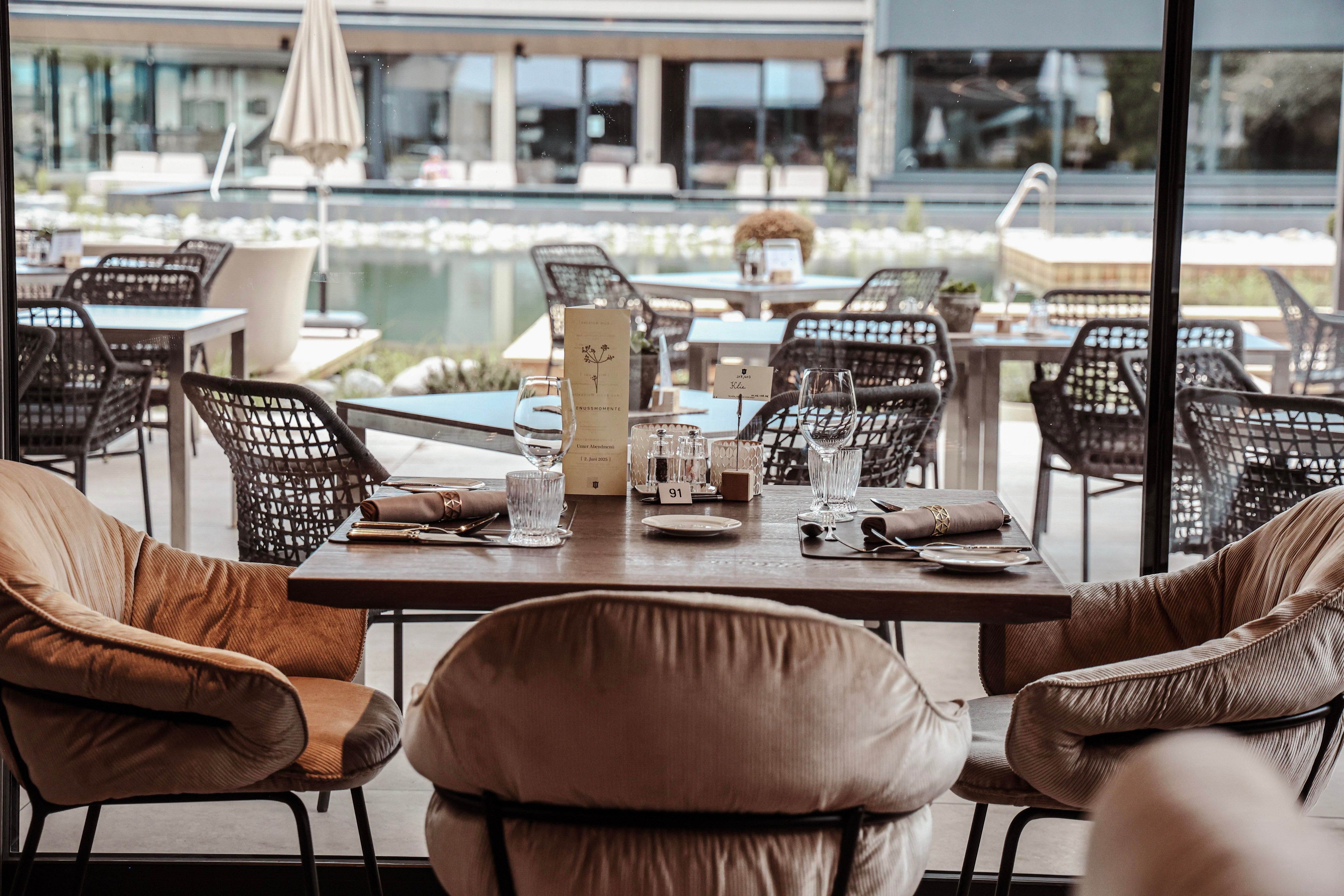 An elegant restaurant with modern chairs and a beautiful view of a pool. The table is attractively set and invites dining.