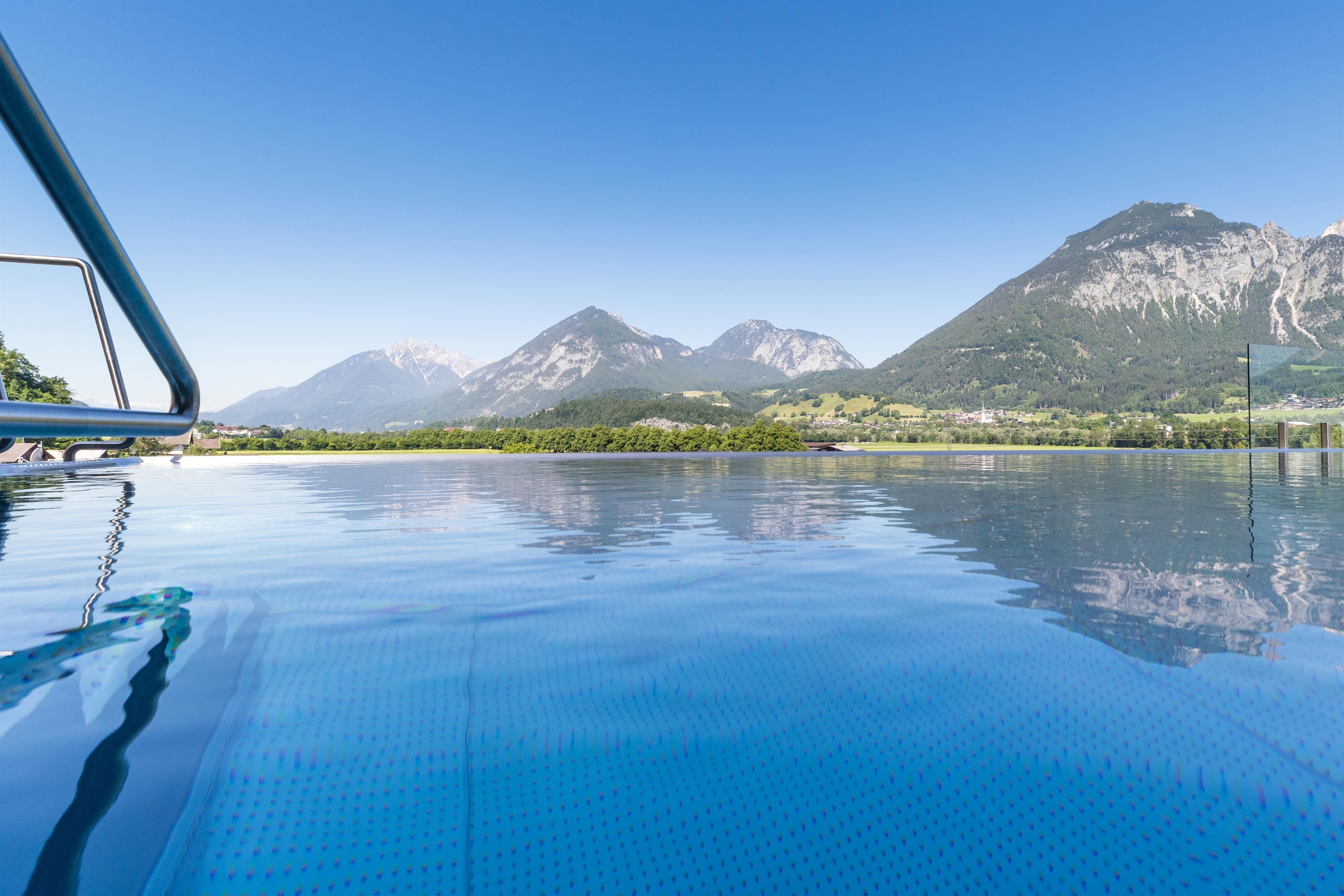 A tranquil pool with clear water, surrounded by impressive mountains. The sky is bright blue and the landscape is very picturesque.