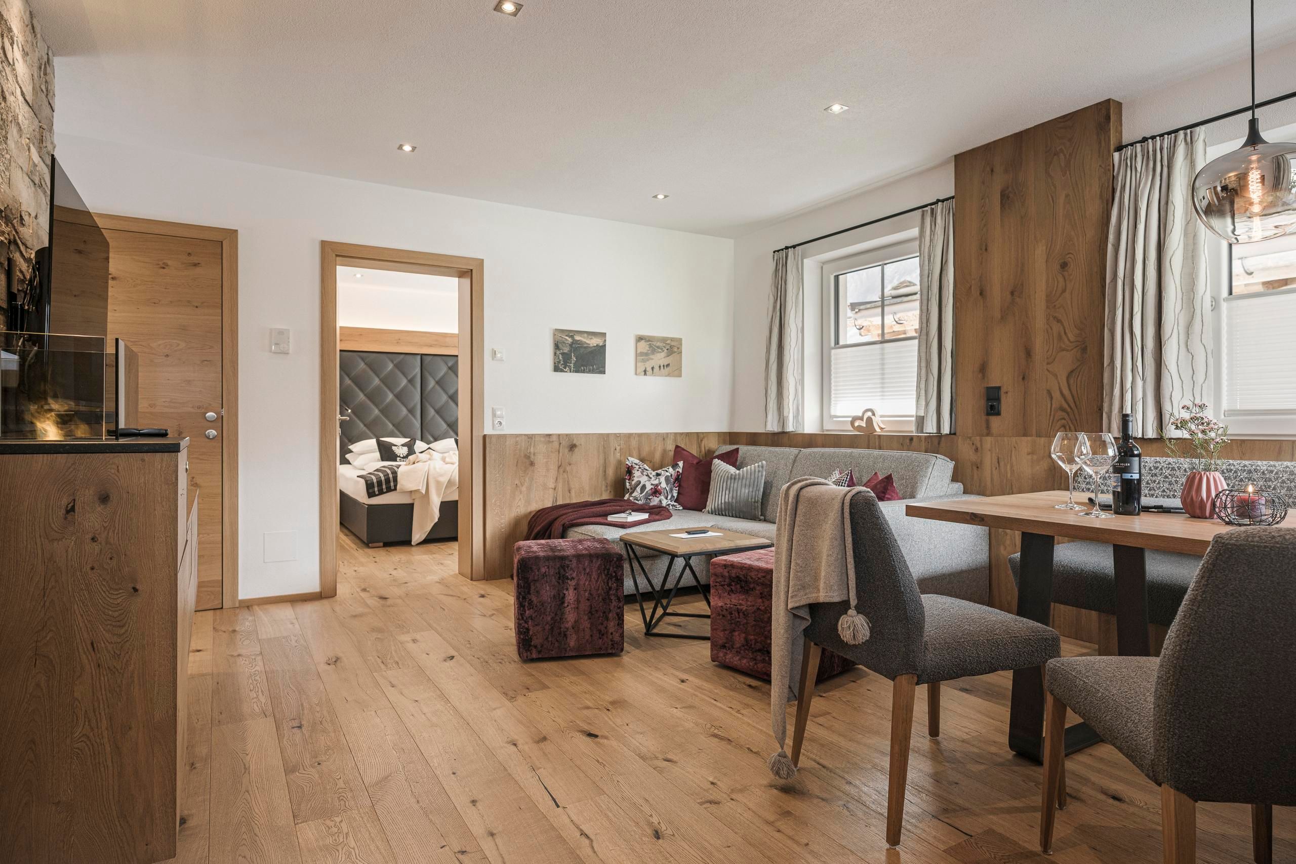 A modern living room with wooden flooring and stylish furniture. In the background, a cozy sleeping area can be seen.