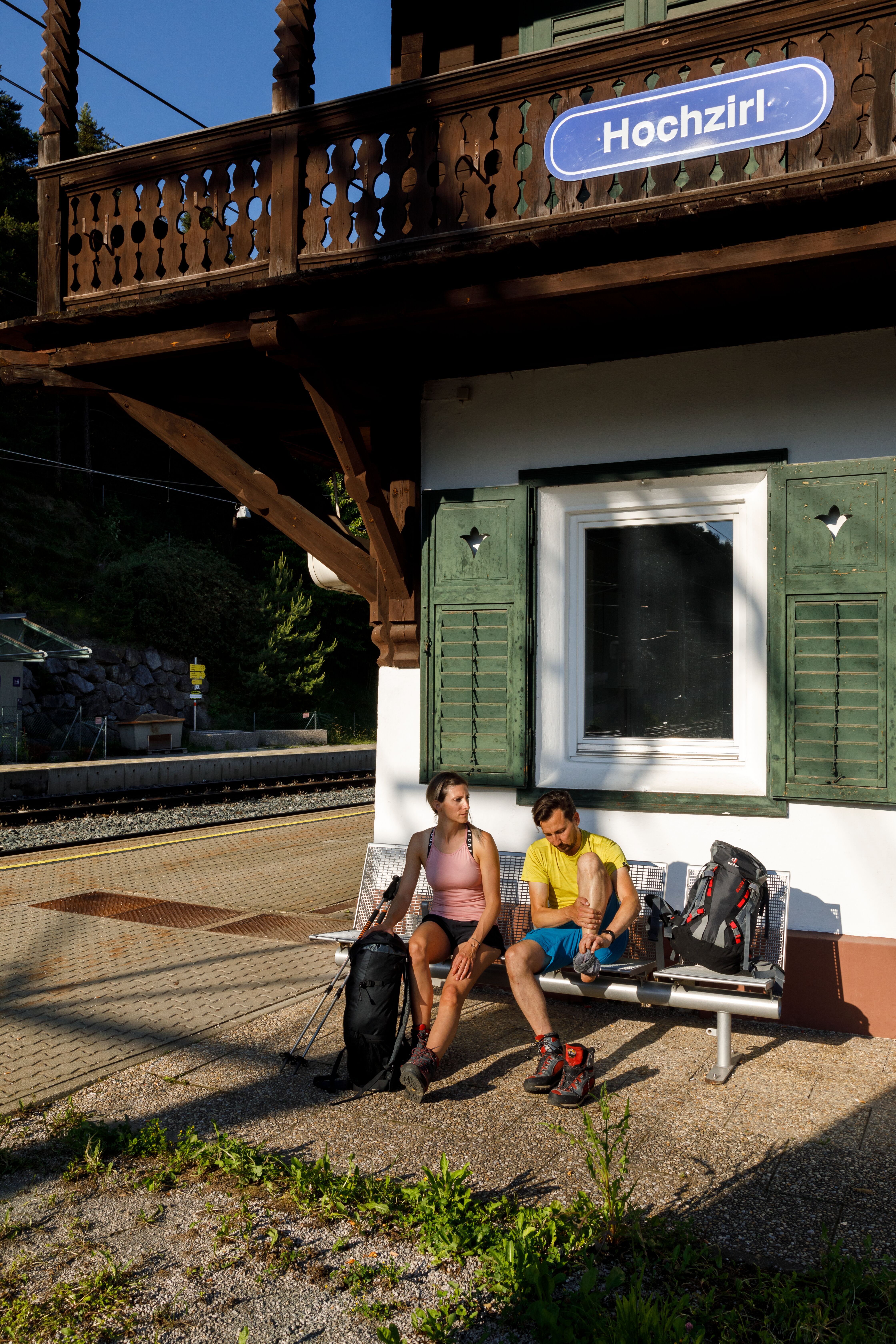 Zwei Personen sitzend auf der Bank vor dem Bahnhof Hochzirl
