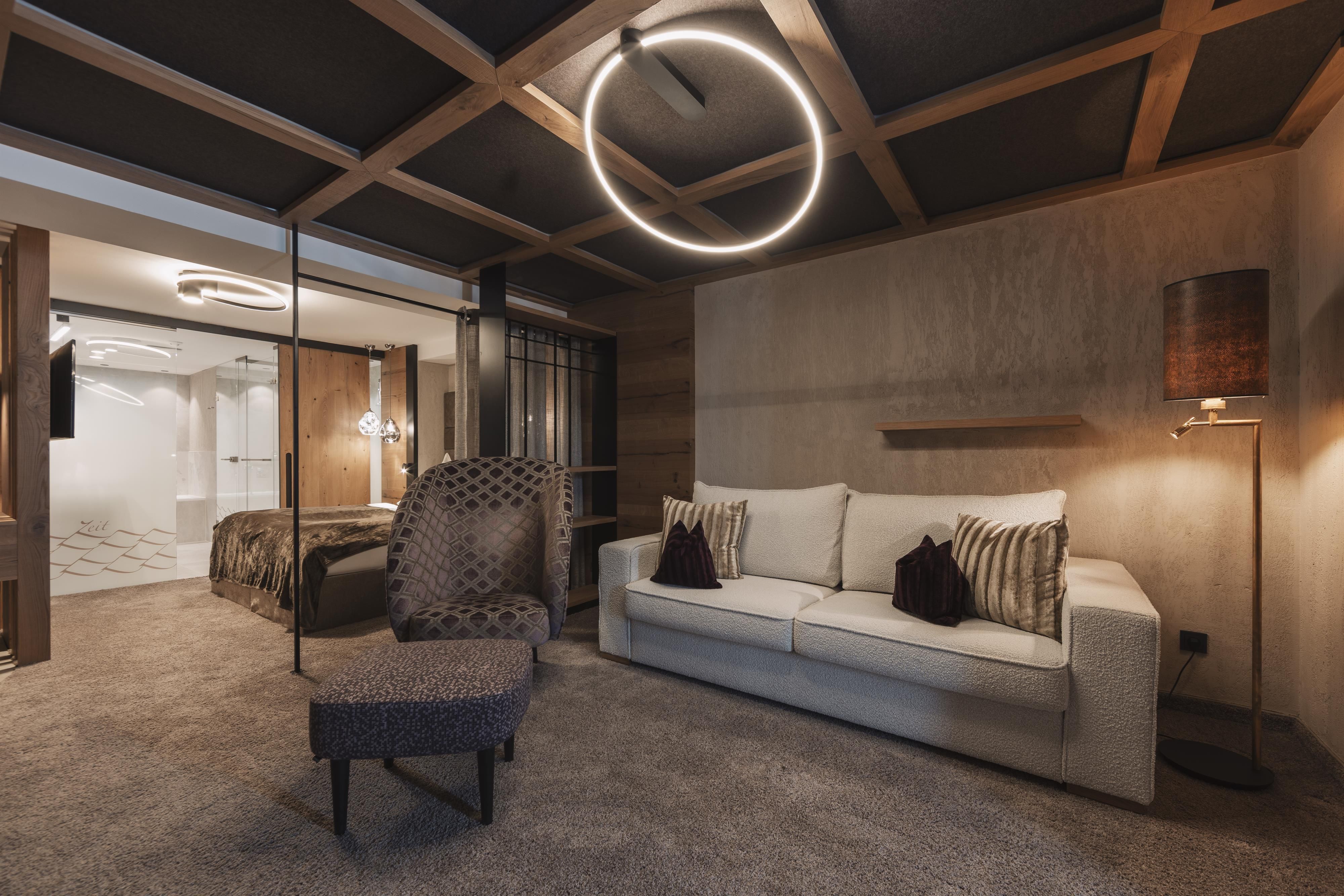 A modern living room with a cozy sofa and a decorative armchair. The ceiling has a stylish design with appealing lighting.