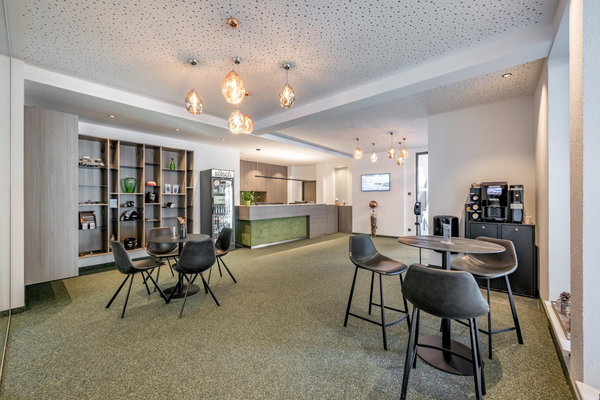 A modern room with a cozy seating area and a coffee station. The pleasant lighting and green carpet create an inviting atmosphere.