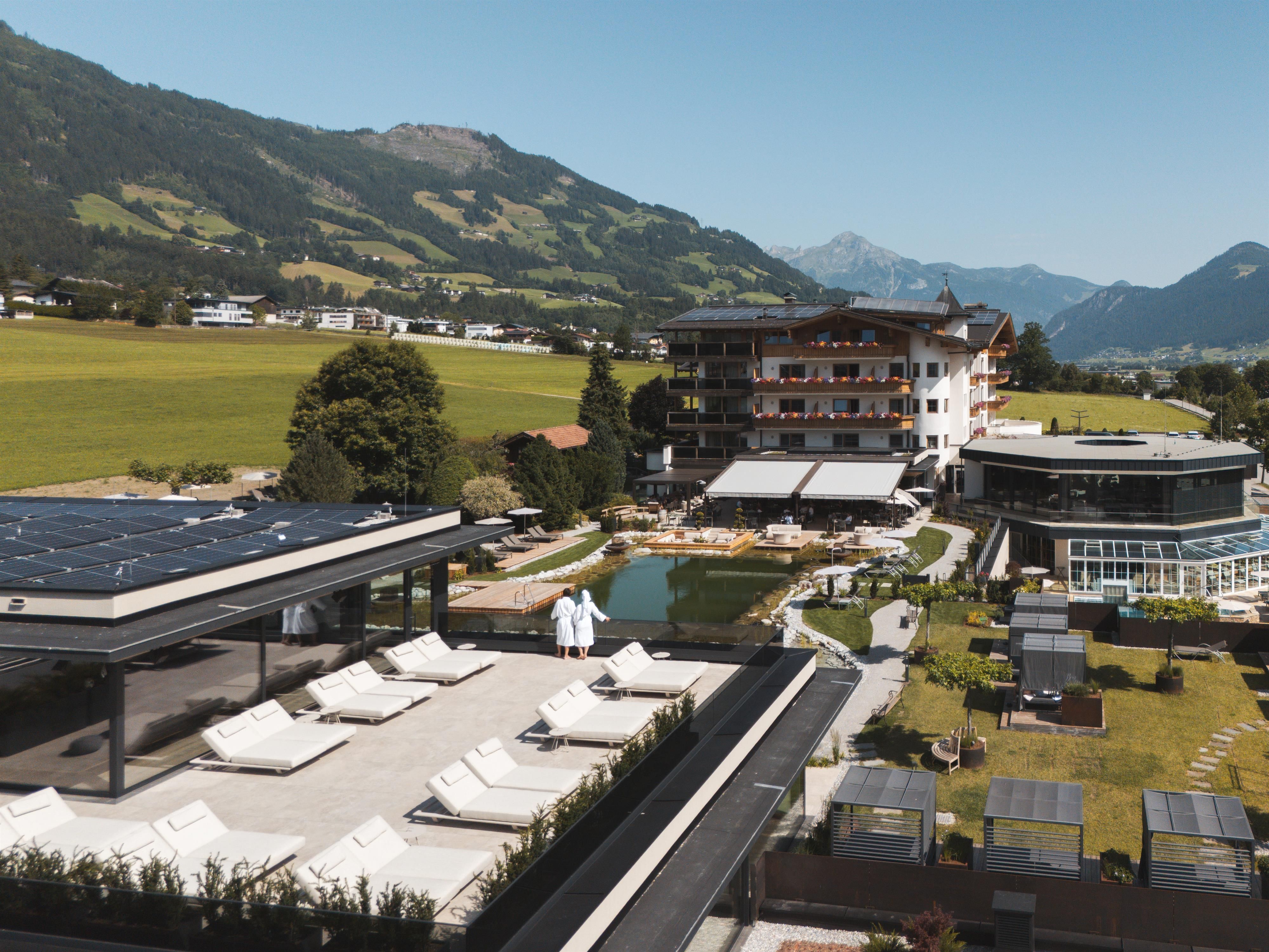 A beautiful hotel in the mountains with a pool and loungers. The landscape is green and the mountains can be seen in the background.