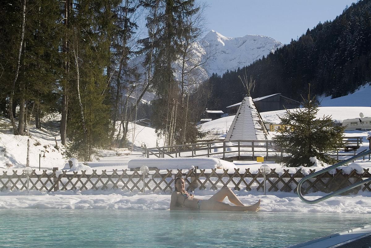 A relaxing swimming pool in the midst of a snow-covered winter landscape. In the background, mountains and a traditional cabin can be seen.