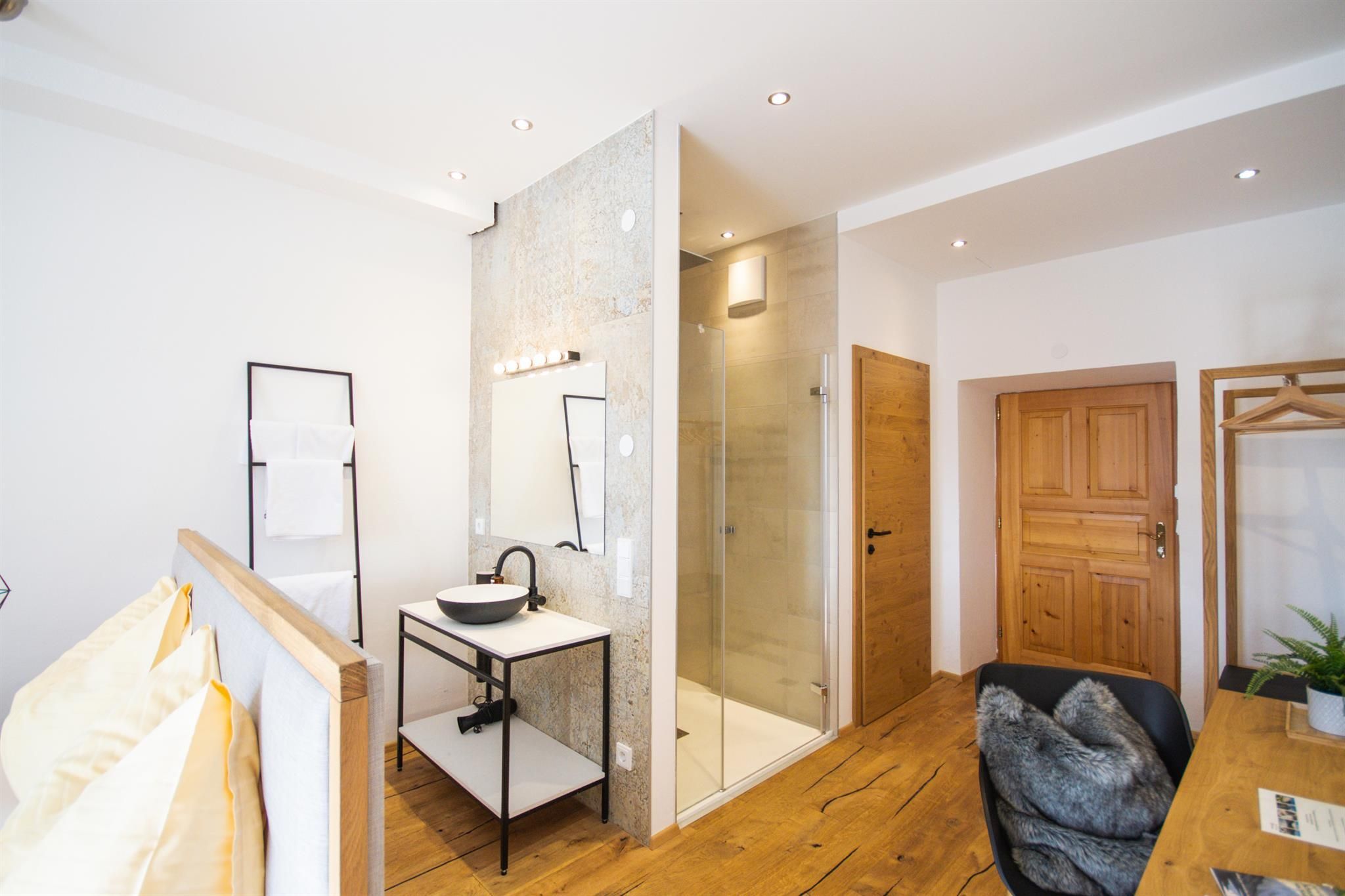 A modern room with a large shower and elegant sink. The wooden floors and bright walls create an inviting atmosphere.