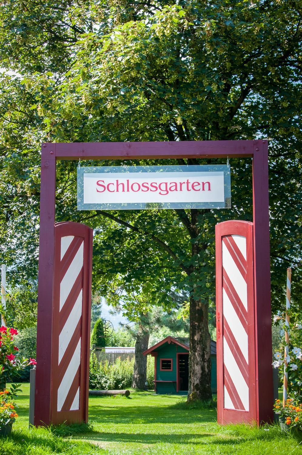 A beautiful entrance to the castle garden with a large sign and colorful flowers. The garden is green and inviting.