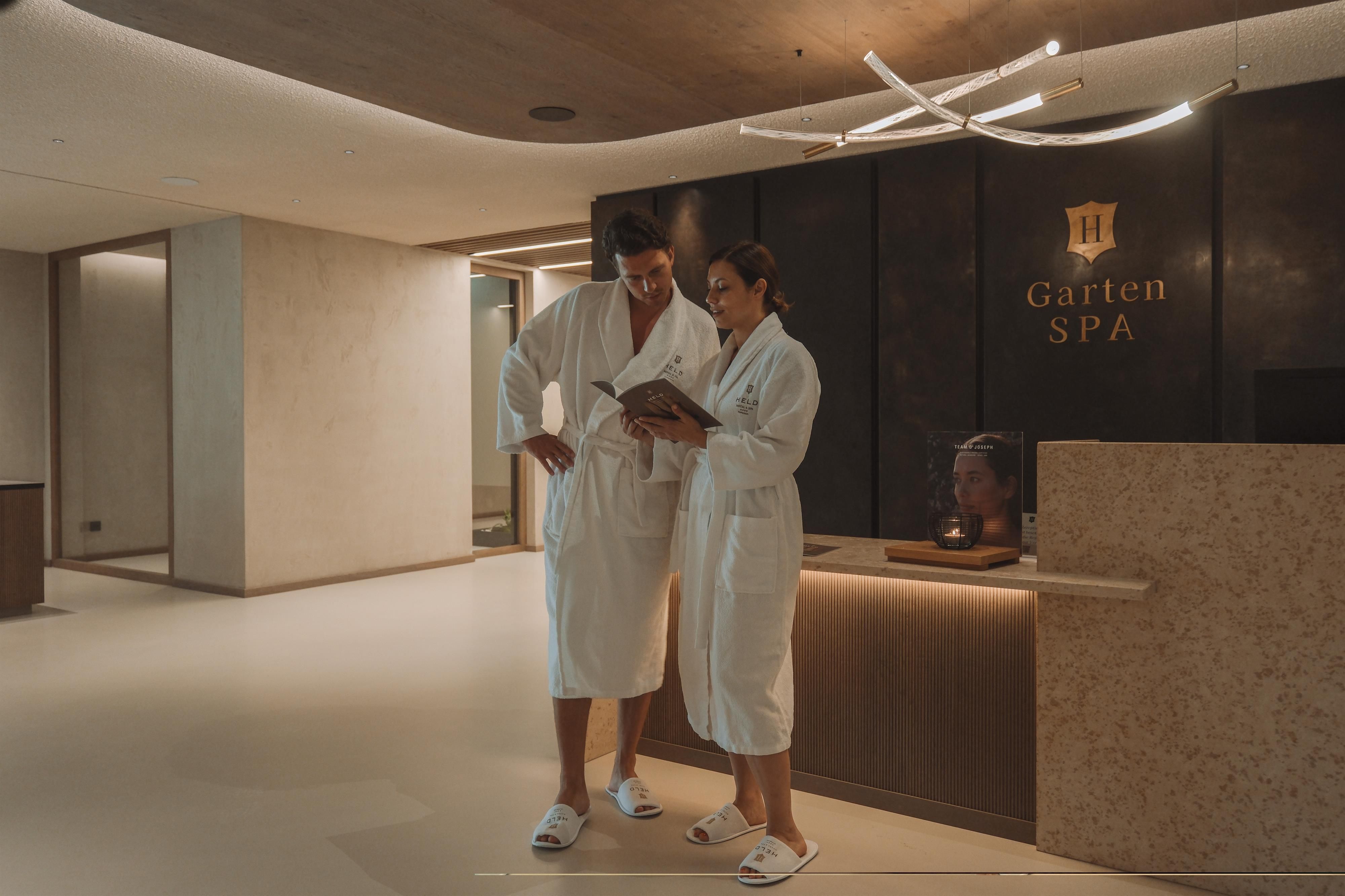 A modern spa with two people in bathrobes looking at a book. The warm lighting creates a relaxing atmosphere.