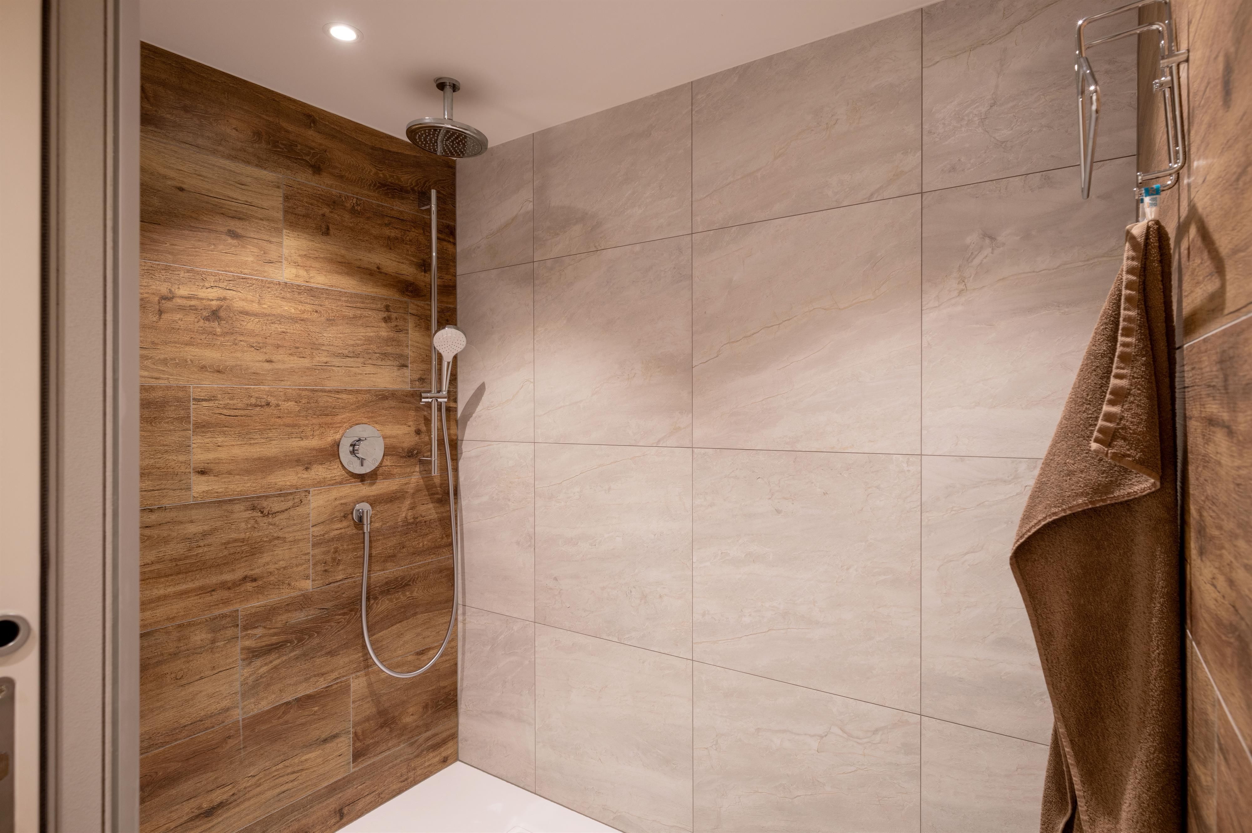 A modern shower with elegant tiles and wooden paneling. A towel hangs on the wall next to the shower.