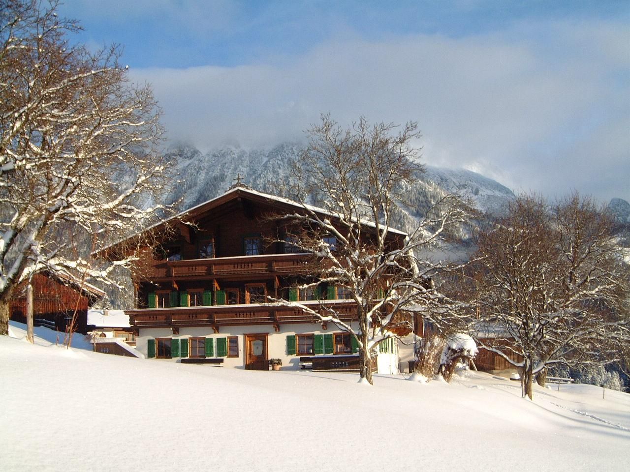 A beautiful chalet in the snowy landscape. In the background, mountains and trees can be seen.