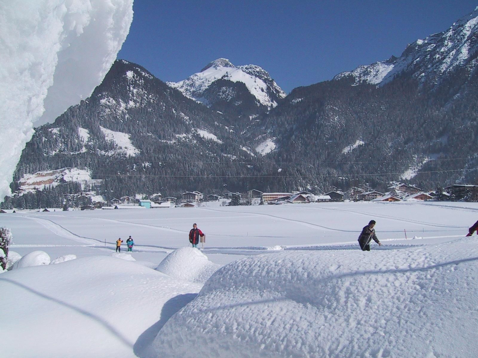 A wintry landscape with snow-covered mountains and people hiking in the snow. The clear, blue sky creates a sunny ambiance.