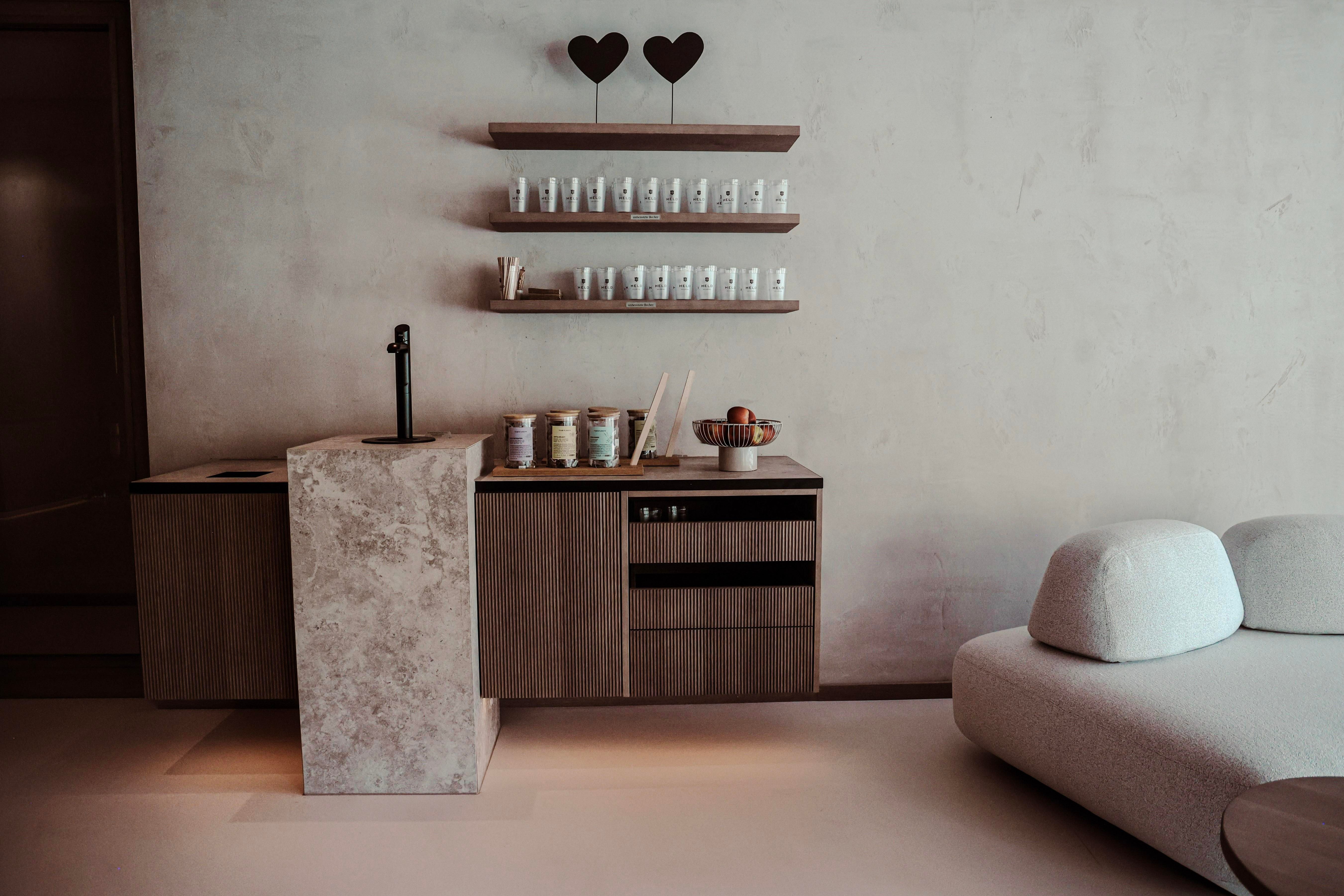 A modern kitchen-living room with an elegant wooden table and a stone surface. On a shelf above are bottles and decorative elements.