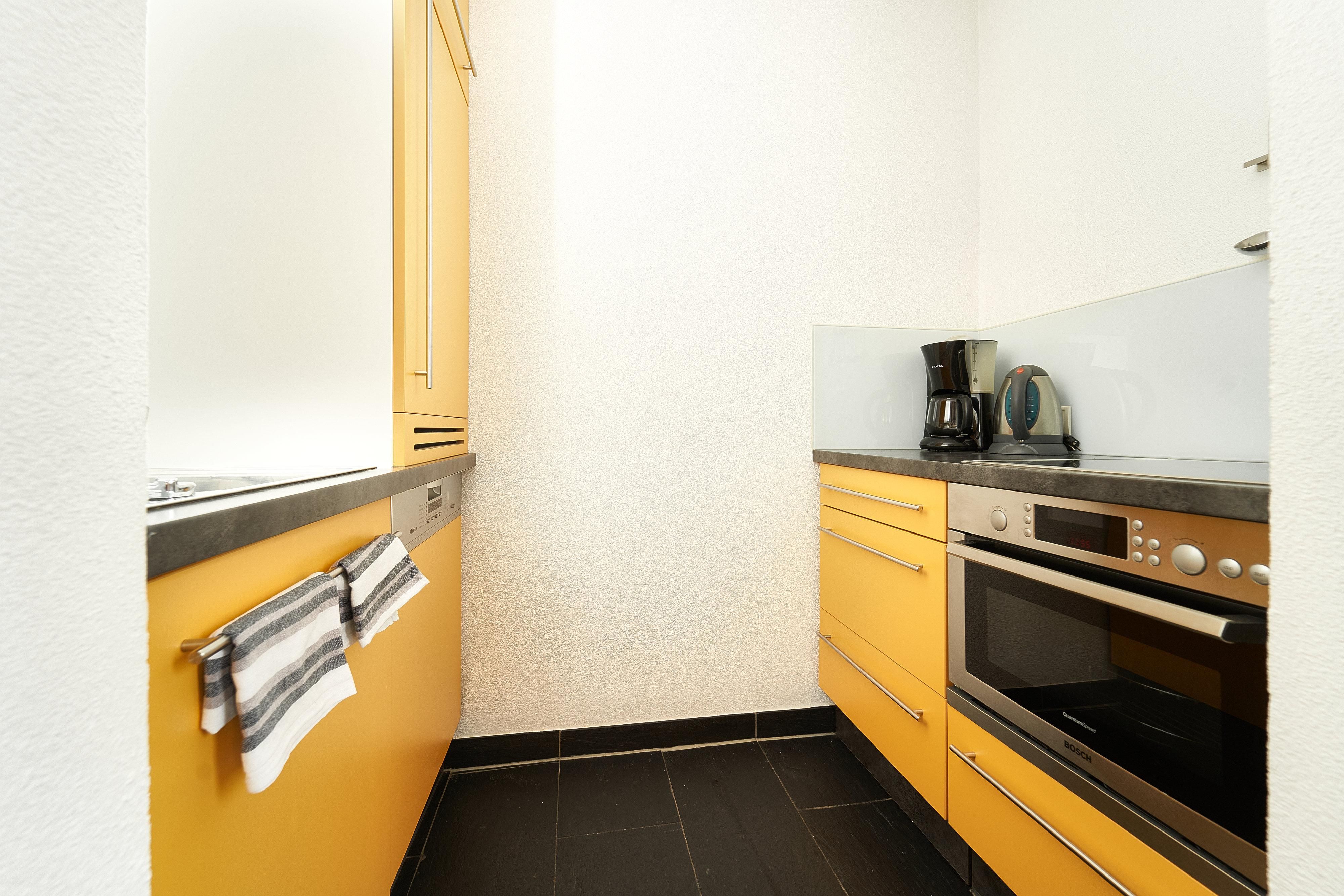 A modern kitchen with yellow cabinets and a black floor. On the countertop, there is a coffee machine and a kettle.