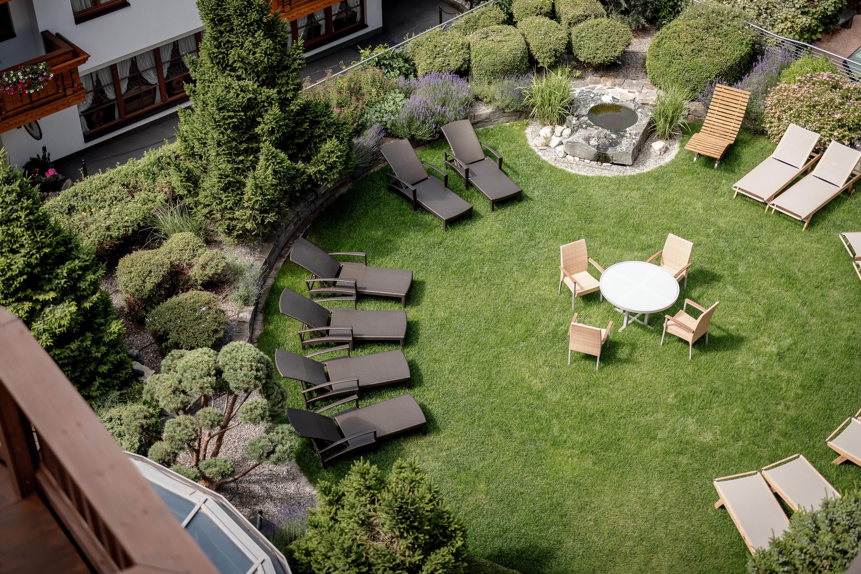 A quiet garden with loungers and a table in the middle. Green plants surround the relaxing atmosphere.