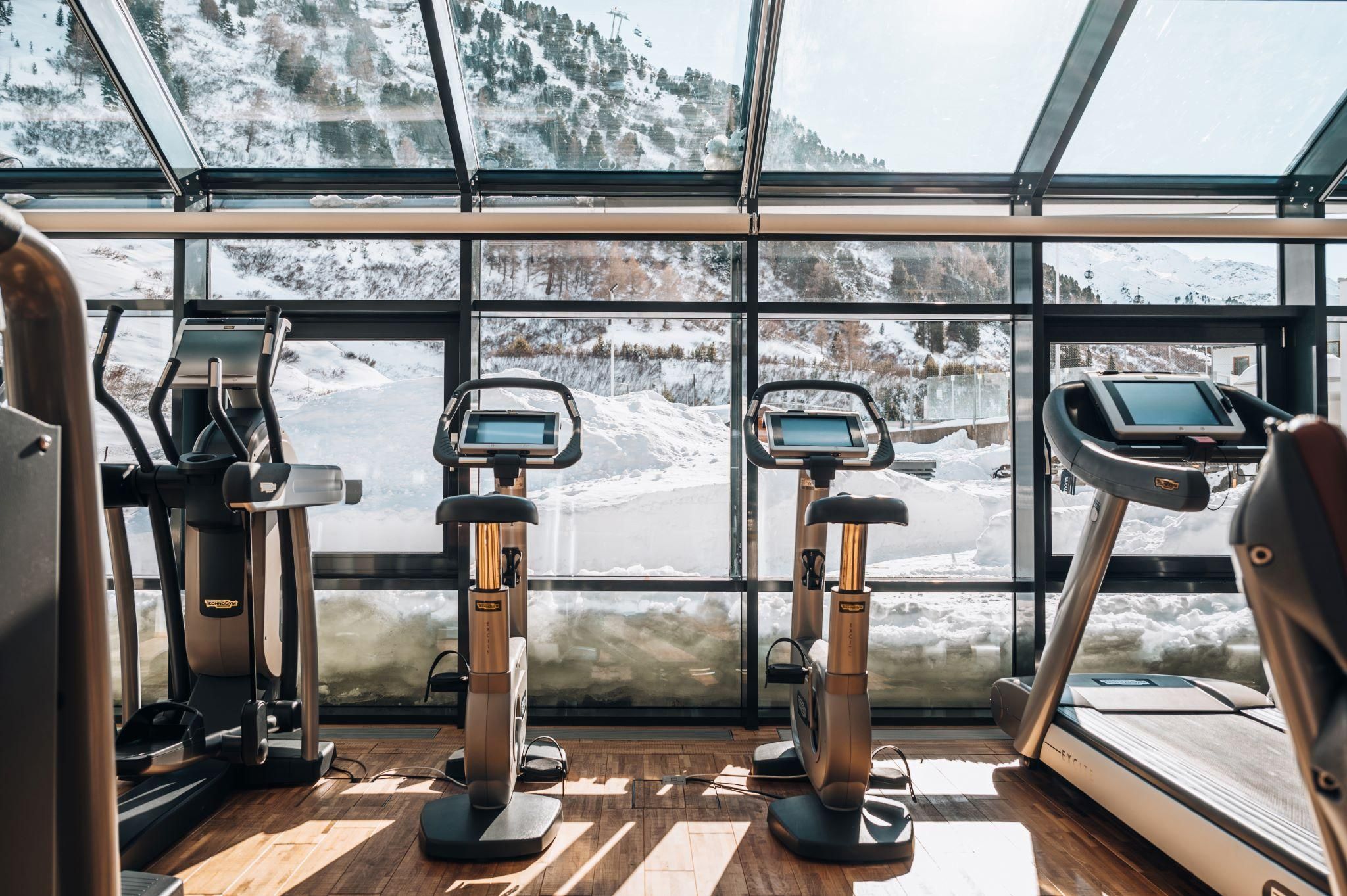 A modern gym with fitness equipment and large windows. Outside, snow covers the landscape.
